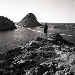 Rear view of woman standing on mountain by sea against clear sky