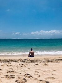 Man sitting on beach against sky