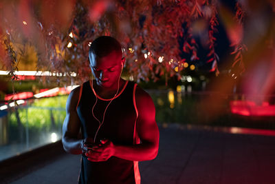 Black sportsman using smartphone under tree