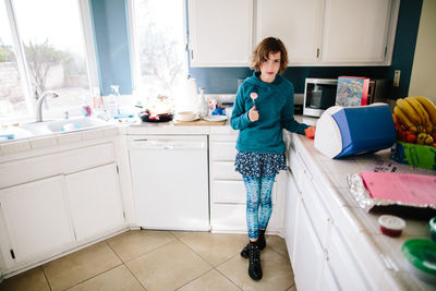 Girl in her kitchen looks toward camera annoyed