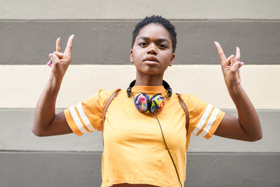 Portrait of young woman gesturing horn sign against wall