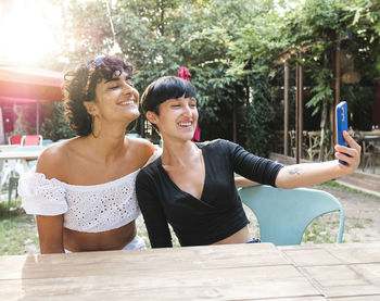 Content friendly multiracial females taking self shot on mobile phone while enjoying weekend together in summer park