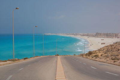 Road by sea against clear blue sky