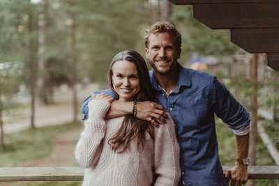 Portrait of smiling couple with arm around standing against railing