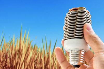 Cropped hand of man holding light bulb against clear sky