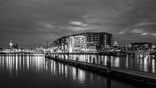 Reflection of illuminated buildings in calm river against cloudy sky