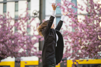 Woman with arms raised throwing flowers standing against building in city