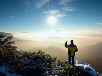 Photographer by smart phone takes picture of misty hilly landscape. exposed rocks covered with snow