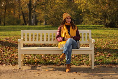 Full length portrait of young woman sitting on bench