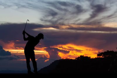 Silhouette man playing golf on field against sky during sunset