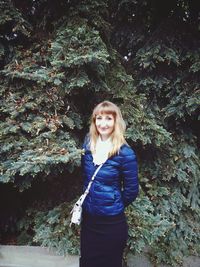 Portrait of smiling woman standing by trees at park