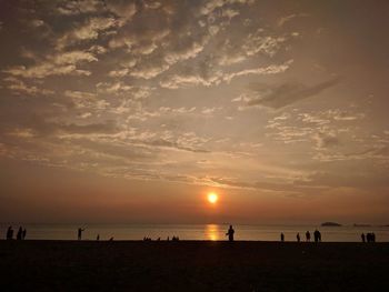 Silhouette people on beach against sky during sunset