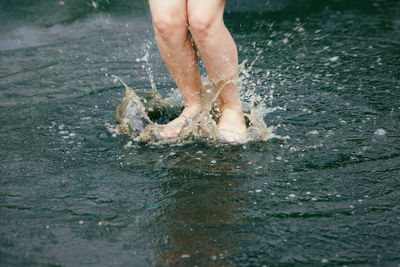 Low section of woman splashing water on lake 