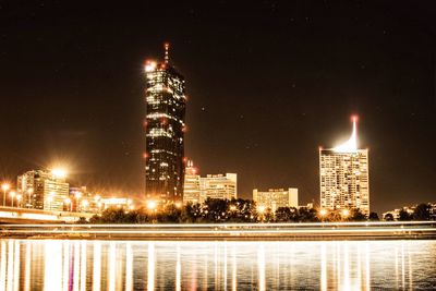 Illuminated buildings by river against sky at night