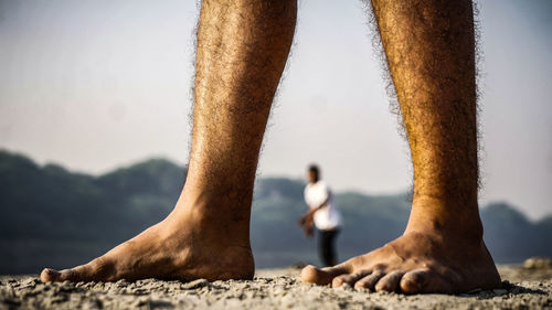 Low section of man standing on beach against sky