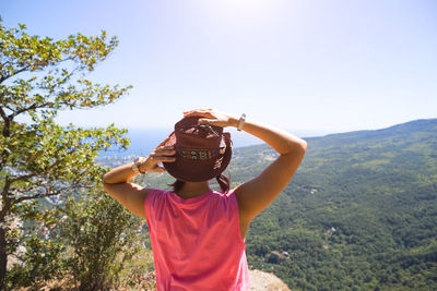 Woman in a hat looks at the panoramic view from the mountain to the sea and the forest. tourist