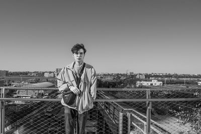 Portrait of man standing by railing against clear sky