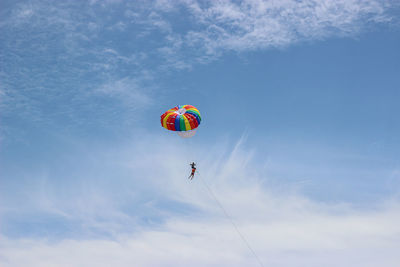 Low angle view of people parasailing against sky