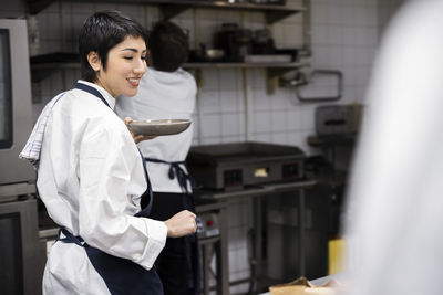 Smiling female chef carrying plate walking in commercial kitchen