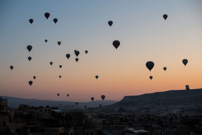 Hot air balloons flying over city against sky during sunset