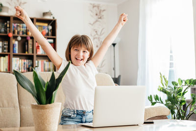 Girl schoolgirl at home in front of a laptop rejoices at success. online learning