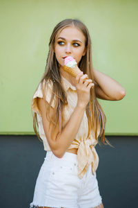 A young beautiful european woman in a beige shirt and white shorts eats ice cream against