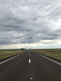 Road passing through field against sky