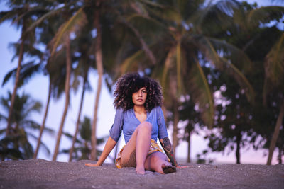 Full length of woman sitting at beach against trees