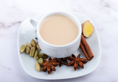 A cup of masala tea on a saucer with spices.