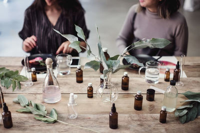 Midsection of young female colleagues sitting at table with various perfume bottles in workshop