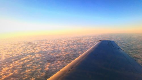 Cropped image of aircraft wing over cloudscape during sunset