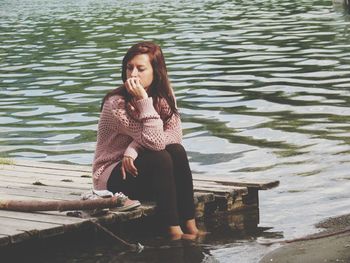 Thoughtful woman sitting on pier at lakeshore