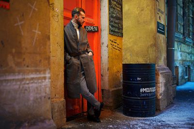 Full length of mid adult man with hands in pockets standing against wall at night