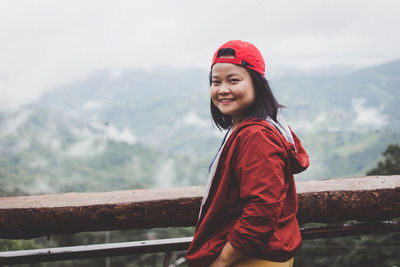 Side view of smiling young woman standing on railing against mountain