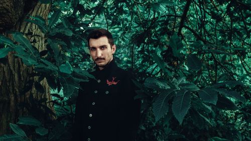 Portrait of young man standing against plants in forest