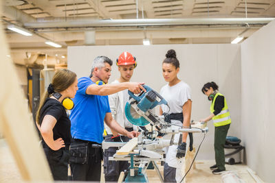 Trainees watching confident male carpenter cutting with electric saw in workshop