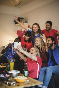 Cheerful friends taking selfie with instant camera while watching sports at home