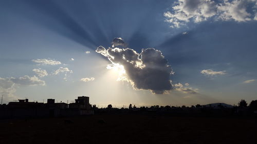 Sunlight streaming through silhouette buildings against sky