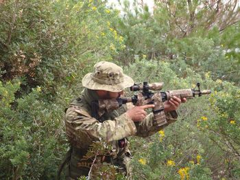 Army soldier aiming machine gun amidst plants in forest