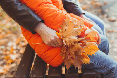 Midsection of person holding orange leaves during autumn