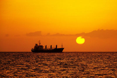 Silhouette ship sailing on sea against orange sky