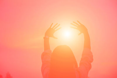 Midsection of woman with arms raised against orange sky