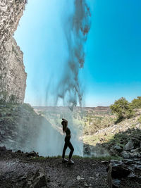 Side view of woman standing against waterfall