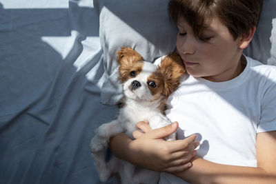 Boy with a dog lies in bed in morning. sleep with pets. cute puppy cavalier king charles spaniel.