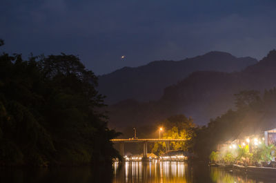 Illuminated bridge over river against sky at night