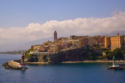 View of cityscape by sea against sky