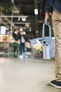 Low section of man carrying grocery basket in supermarket