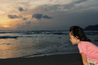 Woman standing at beach against sky during sunset