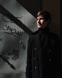 Young man wearing long coat against wall