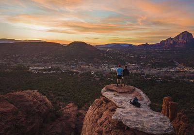 People standing on rock against sky during sunset